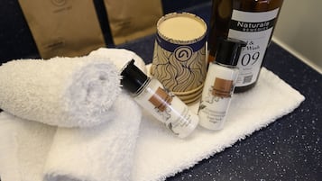 Uma bancada de banheiro com uma toalha branca, um frasco de condicionador, uma vela e um frasco de shampoo.