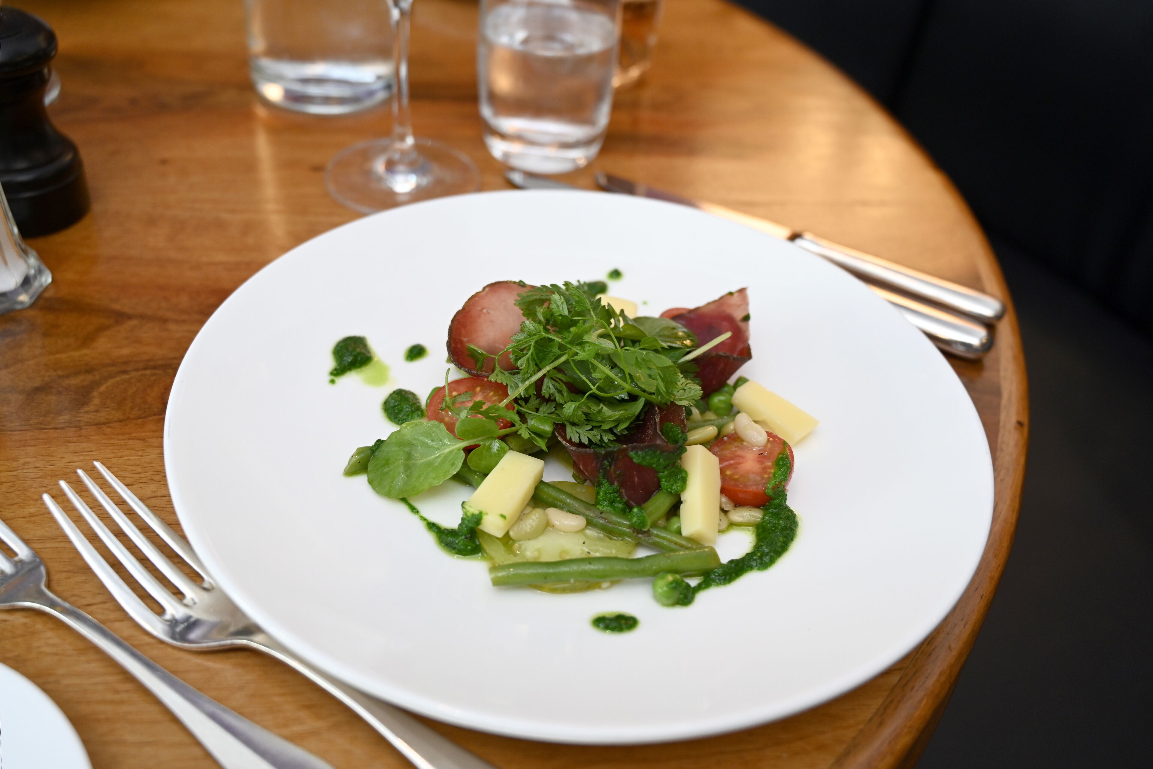 Un plato blanco con ensalada sobre una mesa de madera.