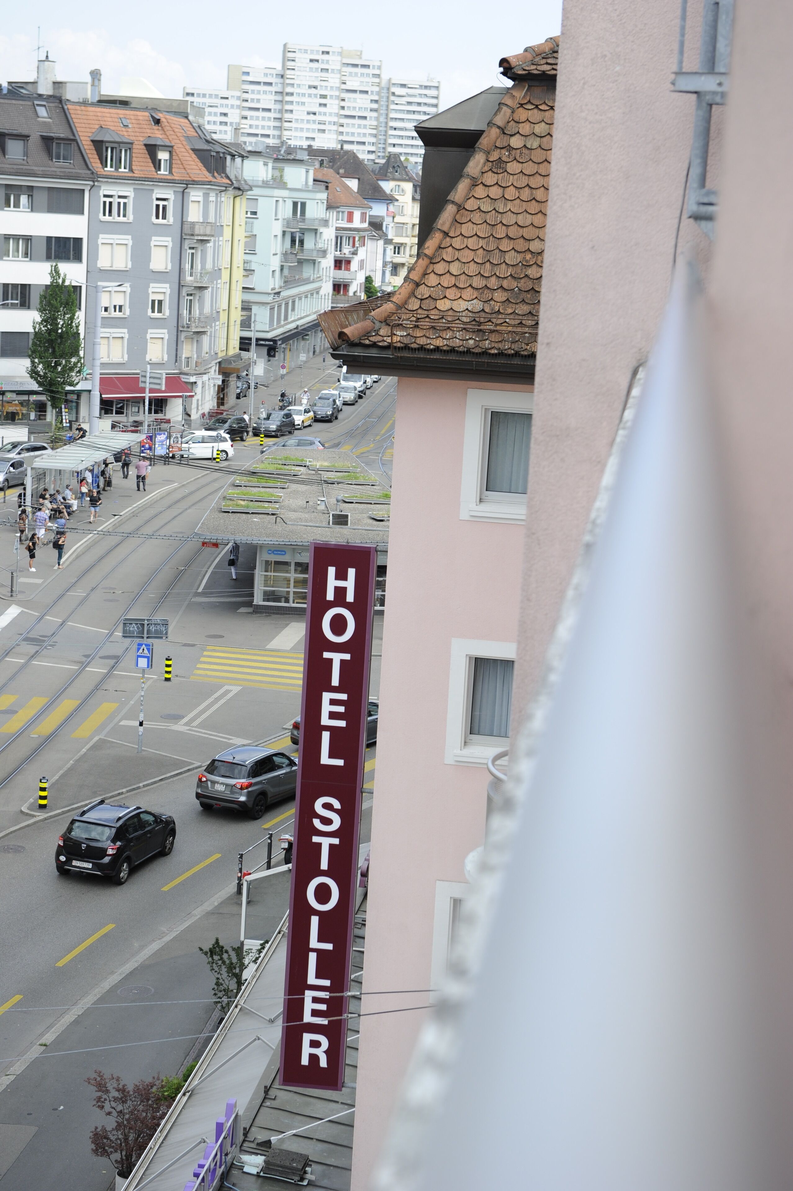 A hotel named "HOTEL STOLLER" with a prominent sign, located in a city with a tram line and buildings in the background.