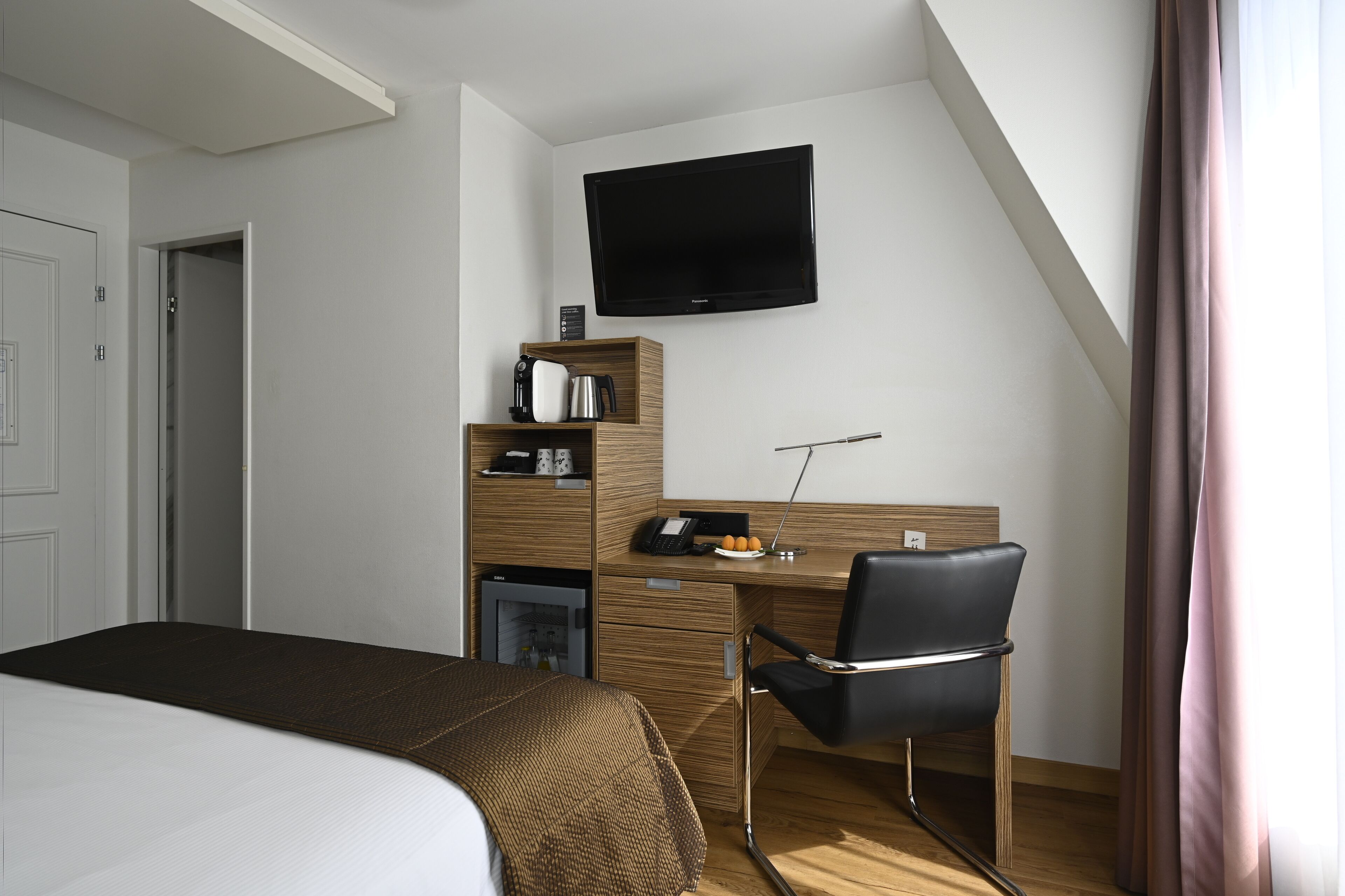 Una habitación de hotel con cama, escritorio, silla, televisor y minibar.