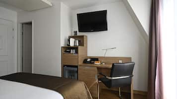 A hotel room with a bed, a desk, a chair, a television, and a minibar.