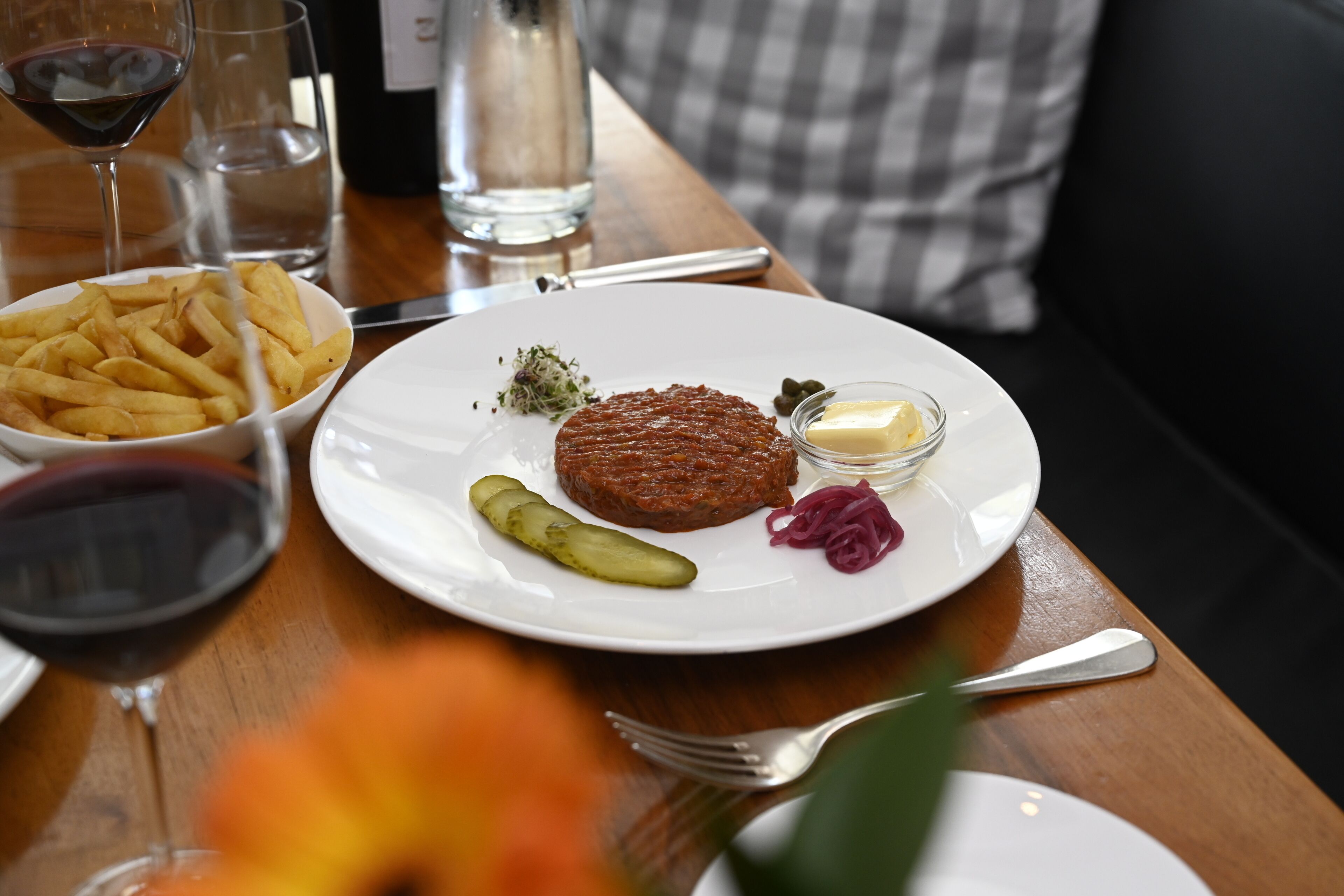 A dining table with a plate of food, including fries, a meat patty, pickles, and a small bowl of sauce.
