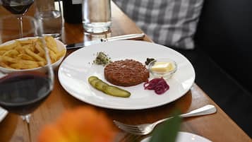 A dining table with a plate of food, including fries, a meat patty, pickles, and a small bowl of sauce.