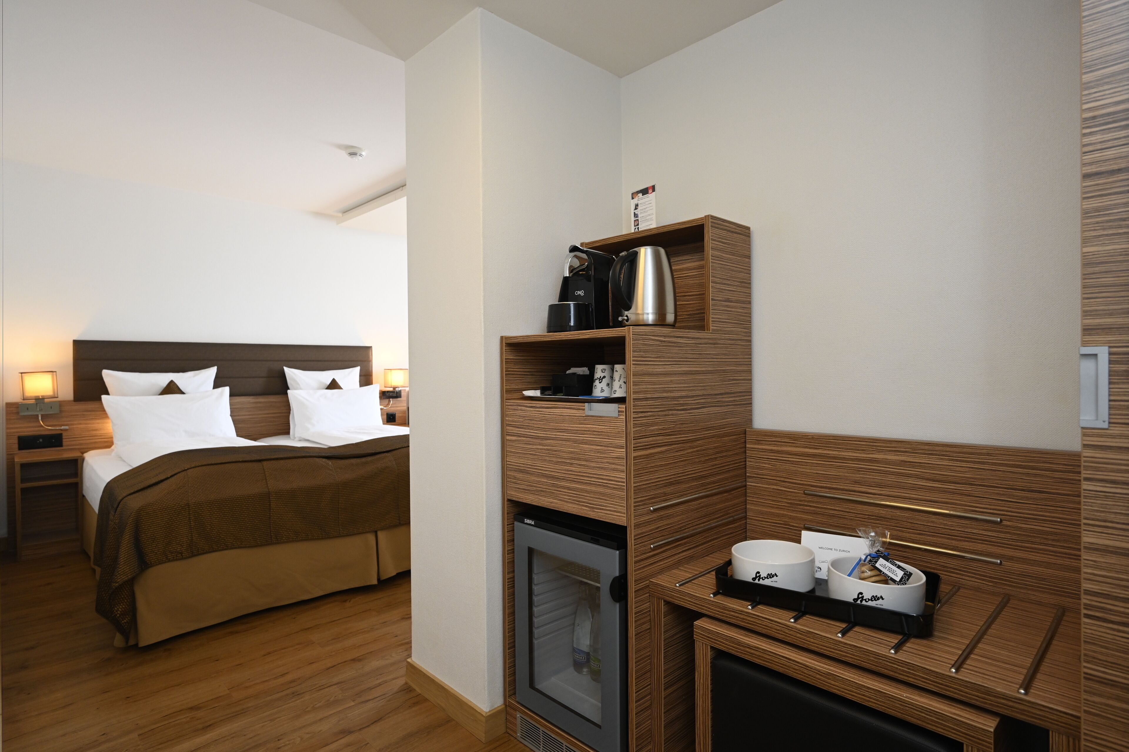 A hotel room with a bed, a minibar, a coffee maker, and a small refrigerator.