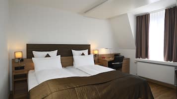 A hotel room with a large bed, two bedside tables, a desk, and a window with curtains.