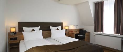 A hotel room with a large bed, two bedside tables, a desk, and a window with curtains.