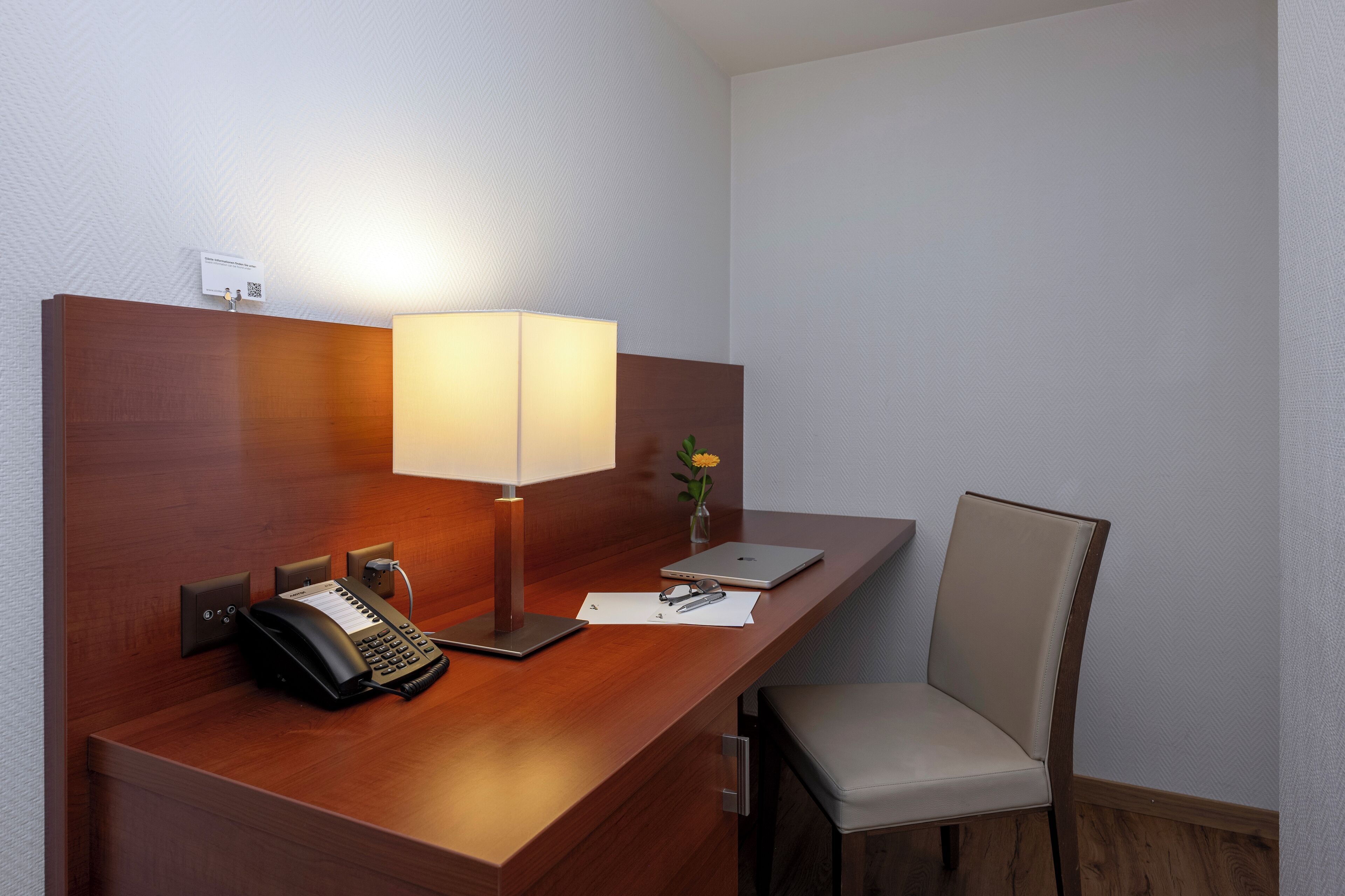 A hotel reception desk with a telephone, a lamp, a laptop, and a chair.
