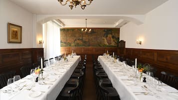 Una larga mesa de comedor con manteles blancos, sillas negras y centros de mesa con velas.