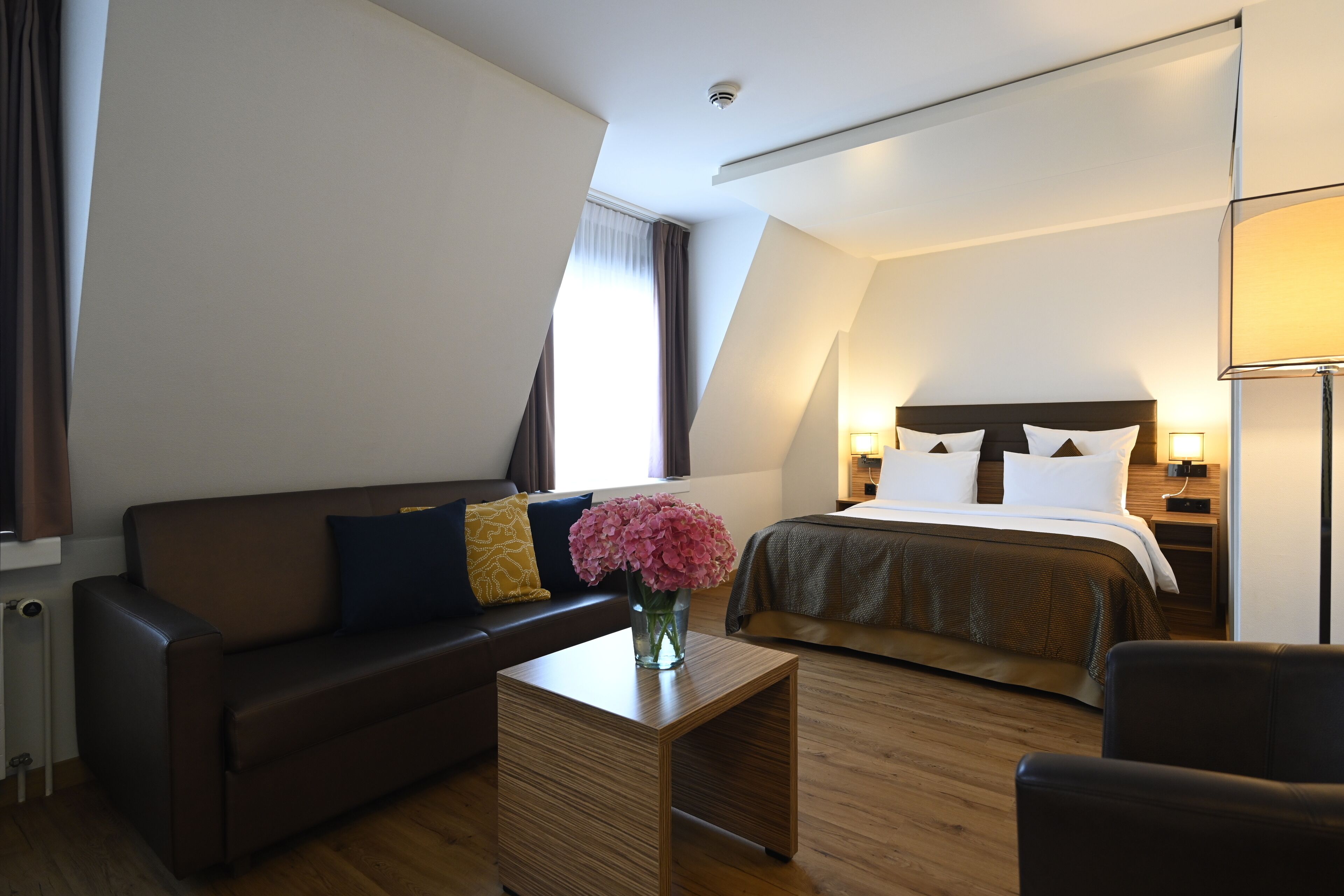 Una habitación de hotel moderna con una cama, un sofá, una mesa de centro y una lámpara.