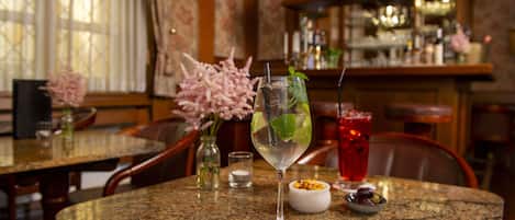Una zona de bar con encimera de granito, un cóctel con adorno de hierbabuena y una bebida roja al fondo.