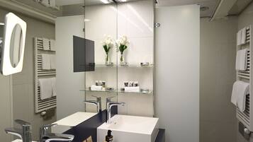 Un baño moderno con dos lavamanos, un espejo grande y un estante de vidrio con artículos de tocador.