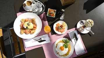 Una mesa con alimentos para el desayuno, como huevos, salmón ahumado y tostadas, además de café y un vaso de zumo de naranja.