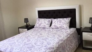 Un lit avec une couvre-lit à motifs, une tête de lit sombre et deux tables de chevet avec des lampes.