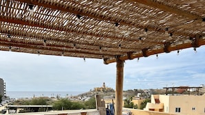 Une terrasse sur le toit, avec une table en bois et des chaises en osier, offrant une vue sur une ville côtière.