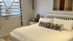 Un lit bien fait, recouvert d’une couette blanche, une table de chevet avec une lampe et un élément décoratif mural.