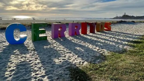 De grandes lettres colorées épellent le mot « CERRITOS » sur une plage de sable, avec de l’herbe.