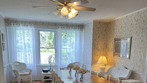 A dining room with a wooden table, white chairs, a ceiling fan, and a window with sheer curtains.