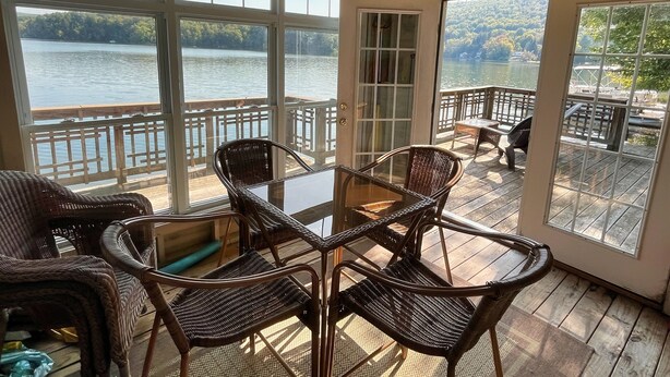 A covered outdoor area with wicker furniture and a glass table, overlooking a lake with a dock and chairs. - Friendship Lodge Total package lake house, tasteful décor, magnificent lakeview (Maryland)