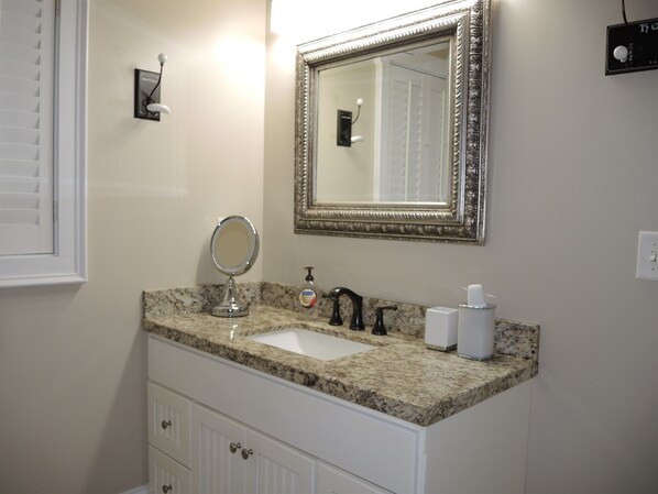 Une salle de bain dotée d’un comptoir en granit, d’un lavabo, d’un miroir, d’un distributeur de savon et d’un distributeur de serviettes.