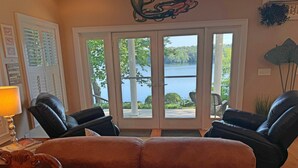 A living room with a large window overlooking a lake, two leather chairs, a wooden sofa, and a decorative wall piece. - Friendship Lodge Total package lake house, tasteful décor, magnificent lakeview (Maryland)