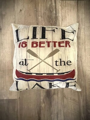 En pude med teksten "Life is better at the lake" og en illustration af en kano.