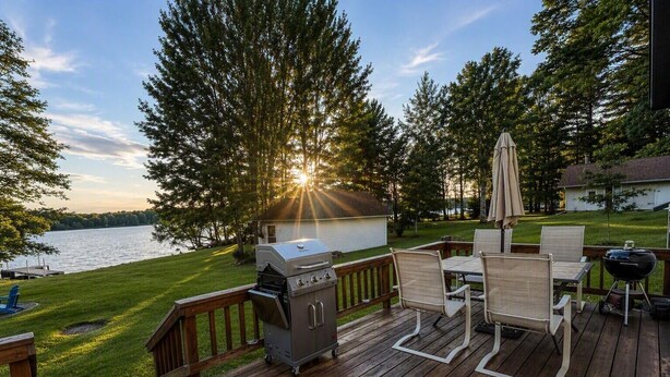 Une terrasse avec un barbecue, des chaises et une vue sur un lac au coucher du soleil.