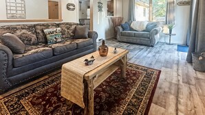 Un salon avec un canapé bleu foncé, une table basse en bois et un tapis à motifs.