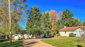 Un chemin de terre menant à une maison avec un toit rouge, entourée d’arbres et d’une pelouse verdoyante.