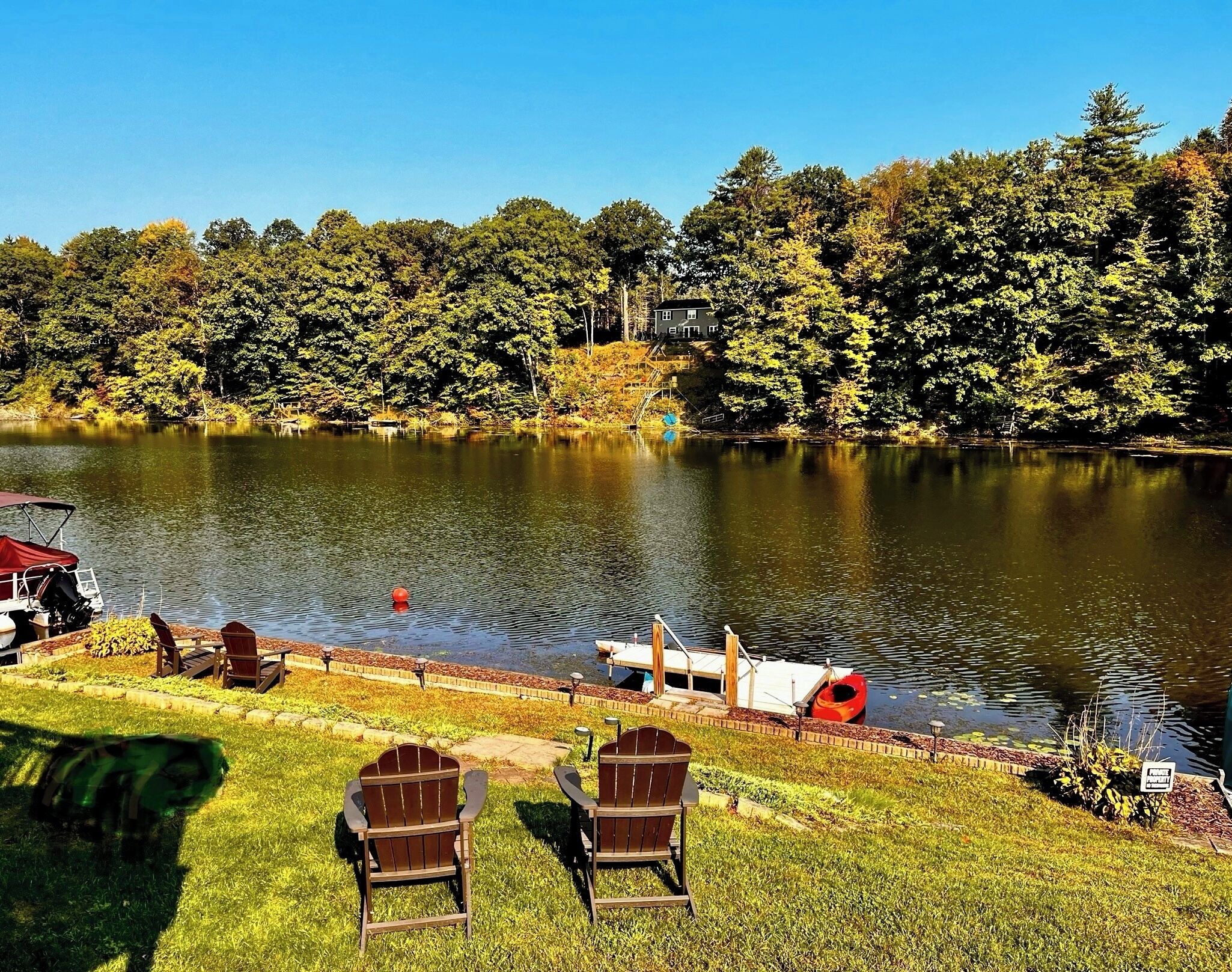 A lakeside view with a dock, chairs, and a house in the background.