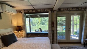 A hotel room with a large bed, a view of a lake, a patio with outdoor furniture, and a "No Smoking" sign.