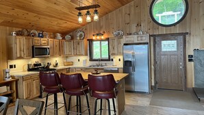 A wooden interior with a kitchen featuring a large island, bar stools, a refrigerator, and a window with a view of greenery. - Lonestar - New build, stunning lake views, near CDP (Milford)