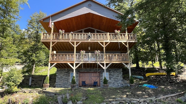 A two-story cabin with a stone foundation, a wooden deck, and a dock extending into a pond. - Lonestar - New build, stunning lake views, near CDP (Milford)