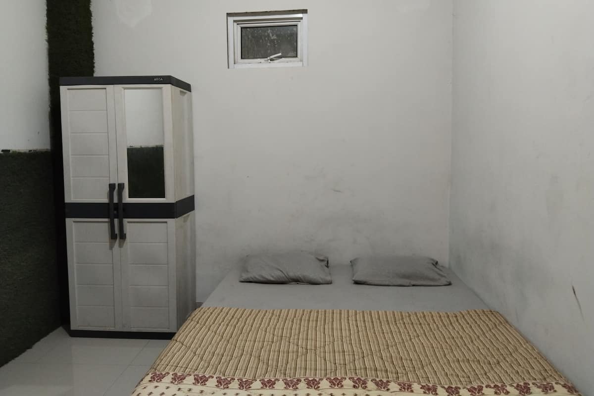 A small, narrow room with a bed, a wardrobe, and a small window.