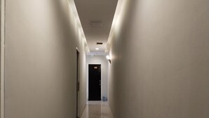 A narrow, well-lit hallway with a trash bin and a door at the end. - The Vinci Hotel powered by Cocotel (Jakarta)