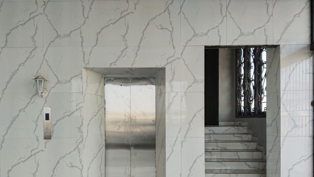 A marble-floored hallway with a central elevator, a staircase to the right, and a wall-mounted light fixture. - The Vinci Hotel powered by Cocotel (Jakarta)