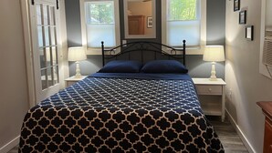 Ein Schlafzimmer mit einem Bett, zwei Nachttischen mit Lampen, einem Fenster mit Jalousien und einer Tür mit Schiebetür.