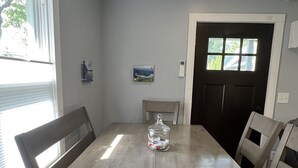 Ein Esszimmer mit Holztisch und -stühlen, einem Glasbehälter mit Snacks und einer Tür mit Fenstern.