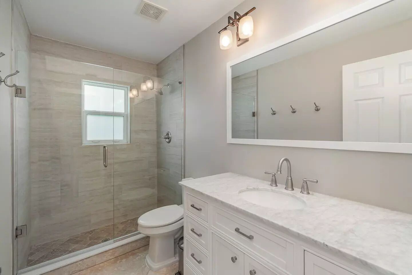 Een moderne badkamer met een douchecabine van glas, een wit toilet en een wastafel met een grote spiegel en meerdere lades.