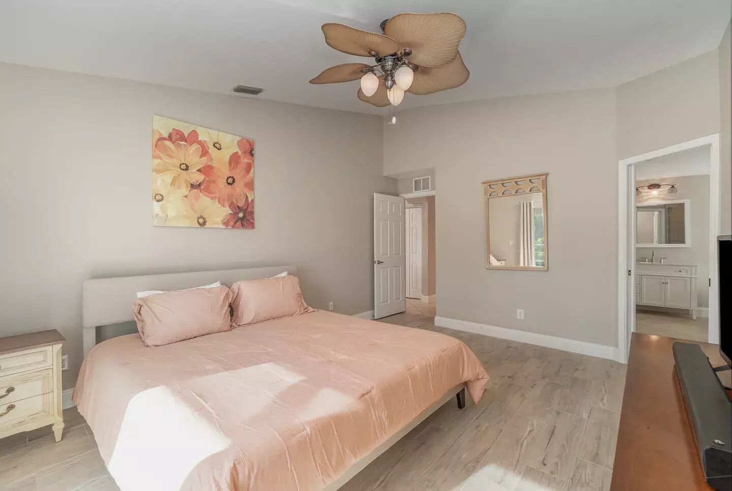 A bedroom with a bed, a ceiling fan, a door, and a bathroom visible through an open door.
