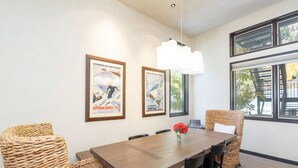 Een eetgedeelte met een houten tafel, rieten stoelen en ingelijste posters aan de muur.