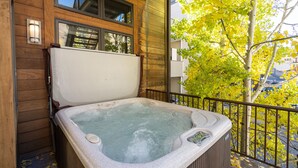 Een hottub met een houten buitenkant, een raam erboven en een boom met gele bladeren op de achtergrond.