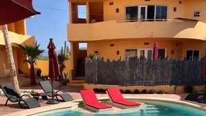 Una piscina con sillas de sol rojas y una valla de madera al fondo.