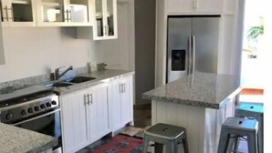 Una cocina moderna con armarios blancos, un refrigerador de acero inoxidable y una encimera de granito.