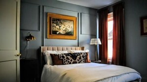 A neatly arranged bedroom with a bed, a nightstand, a lamp, and a painting on the wall. - Cleveland Hideaway on Clifton (Cleveland)