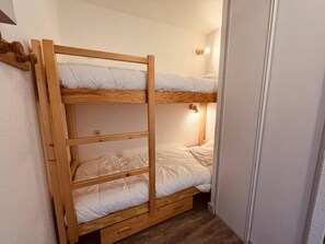 A bunk bed with three levels, a small drawer, and a wall-mounted light.