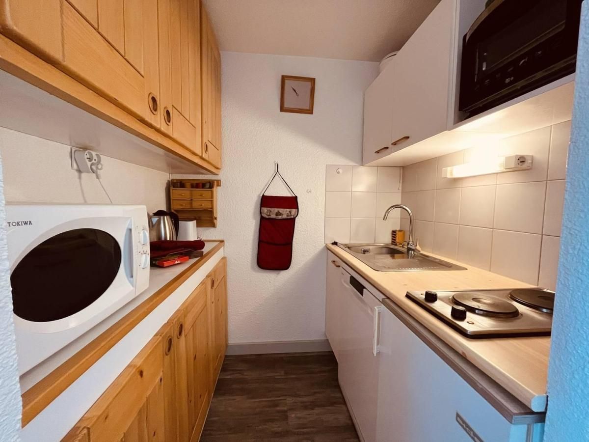 Una cocina compacta con armarios de madera, un microondas blanco, un lavamanos y una estufa.