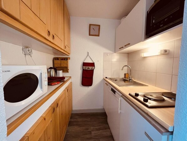 A compact kitchen with wooden cabinets, a white microwave, a sink, and a stove.