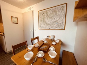 A dining table set for four with white dishes and cutlery, a map on the wall, and a small framed picture on the wall.