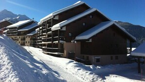 En rad av träbyggnader i chaletstil med balkonger, med snötäckta berg som bakgrund.
