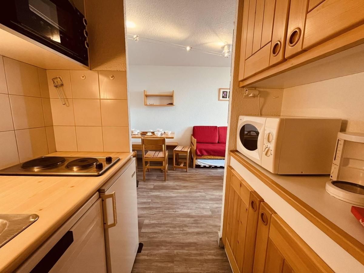 Cocina compacta con estufa, microondas y comedor con sofá rojo.